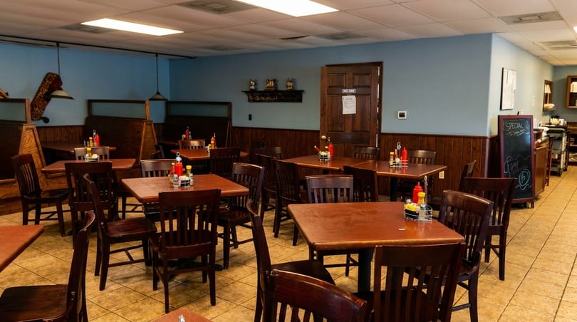Empty restaurant interior with wooden tables, chairs, and booths, featuring light blue walls and wood paneling.